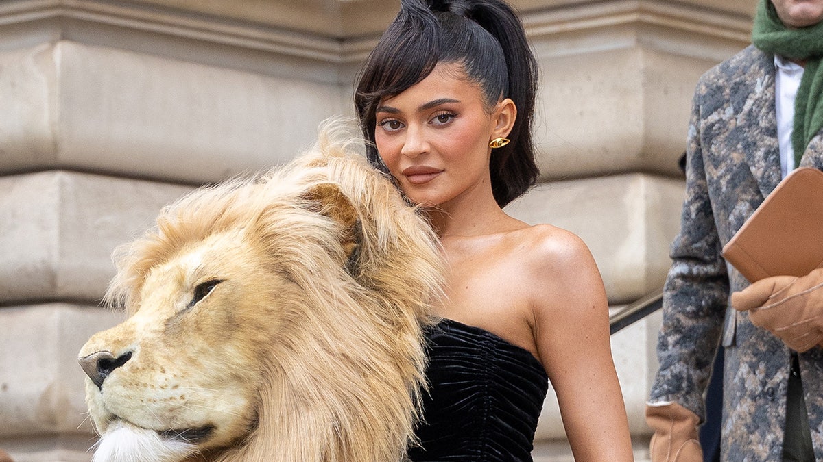 Kylie Jenner em Paris França usando um vestido preto com uma grande cabeça de leão caindo em cascata pelo vestido e no ombro direito