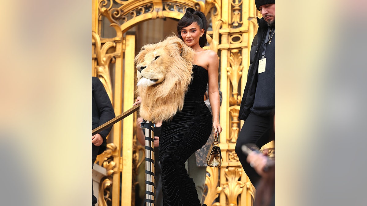 Kylie Jenner cascades down stairs in Paris at the Schiaparelli Haute Couture Spring Summer 2023 show wearing a black gown with a large embroidered lion head