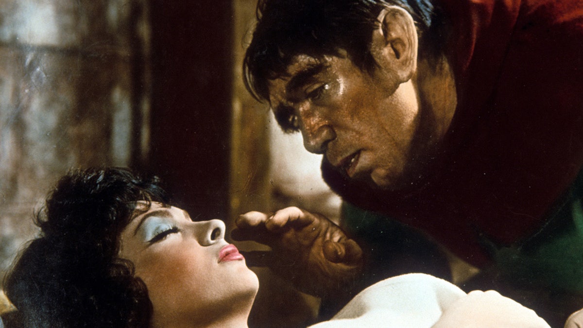 Gina Lollobrigida with bright blue eye shadow sleeps and is approached by Anthony Quinn in a scene during "The Hunchback of Notre Dame"