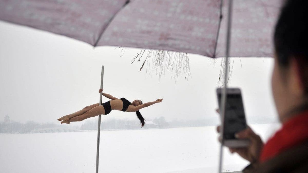 A woman taking a photo of a pole dancer practicing after it snowed in Tianjin during a promotional event by members of China's national pole dancing team and students of the sport.
