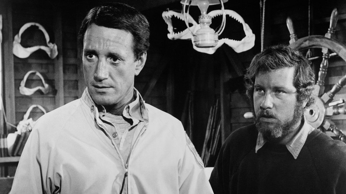 In a black and white photo, Roy Scheider and Richard Dreyfuss look perplexed while filming a scene from "Jaws"