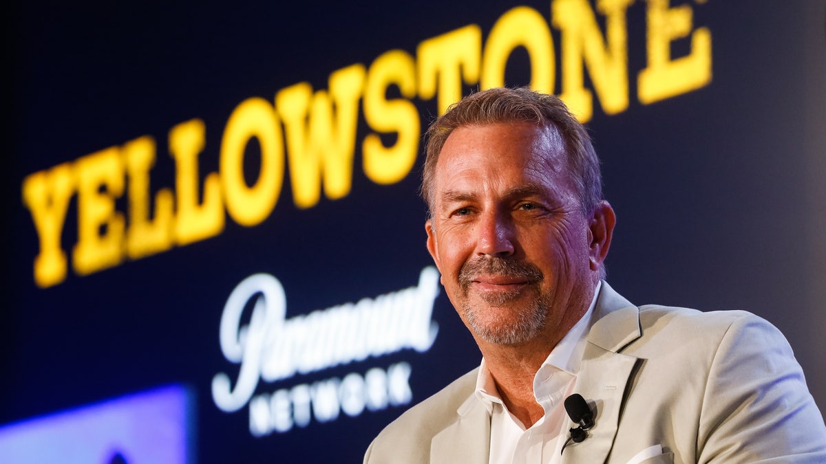 Kevin Costner in front of a sign for "Yellowstone"