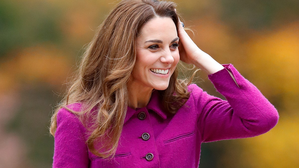 Kate Middleton smiling while wearing a purple dresscoat