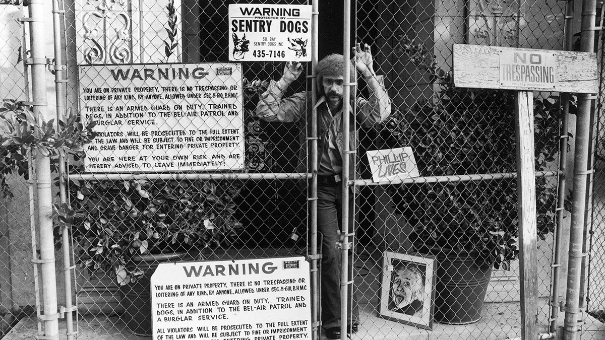 Phil Spector peers through the fence gates at his Beverly Hills estate
