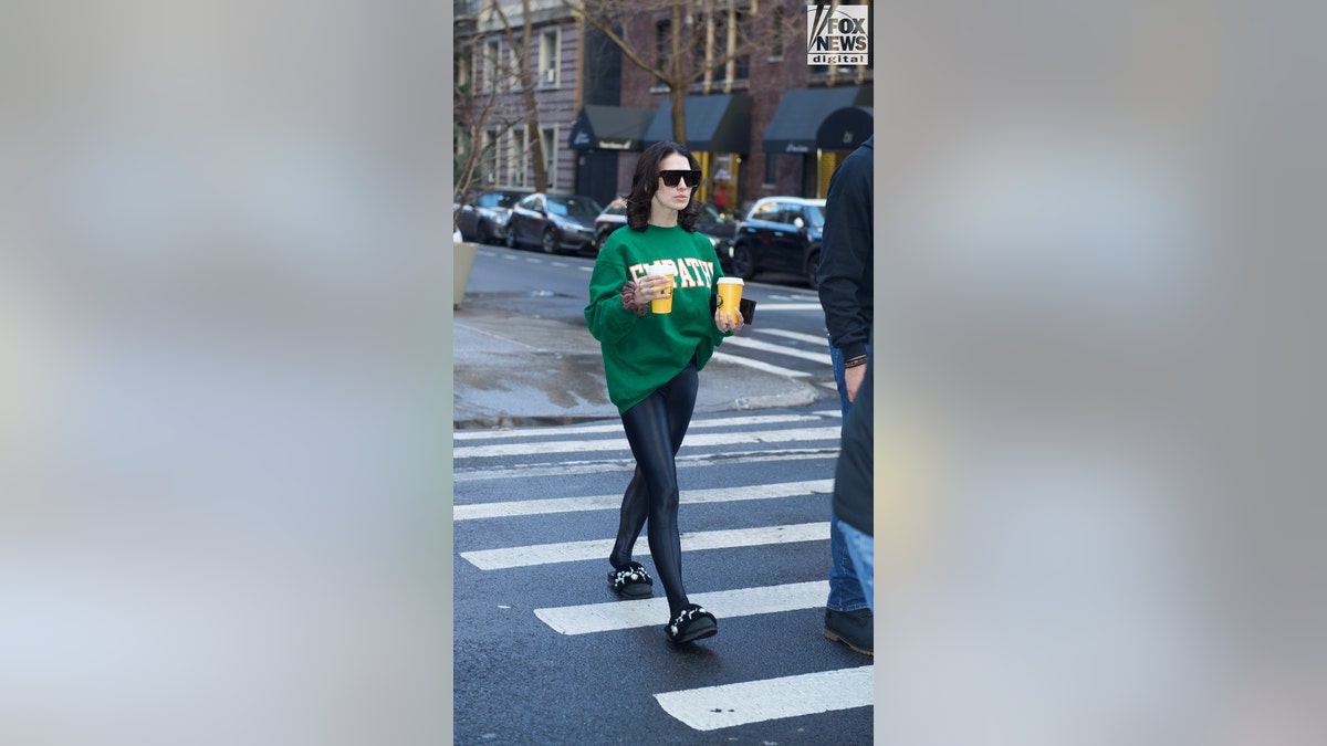 Hilaria Baldwin walks across a crosswalk carrying two cups of coffee.