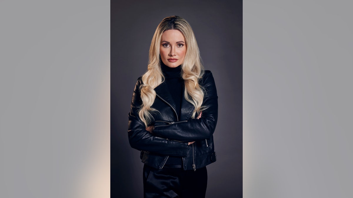 Holly Madison standing wearing a leather jacket and looking serious