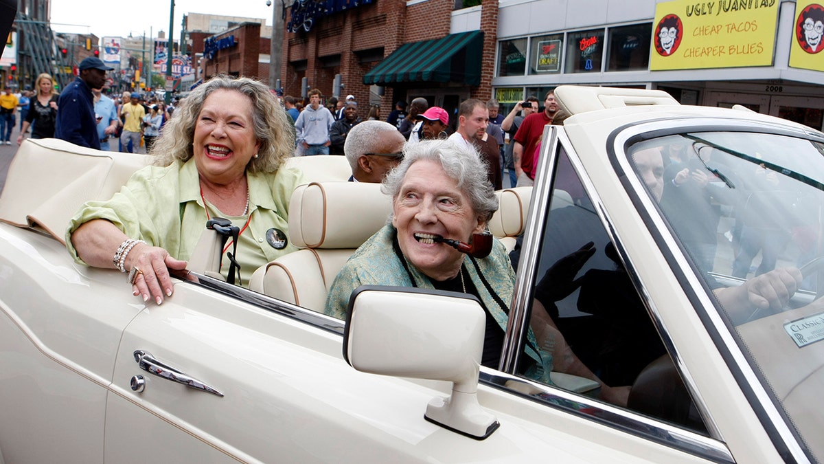 Jerry Lee Lewis with a pipe rides in a white convertible.