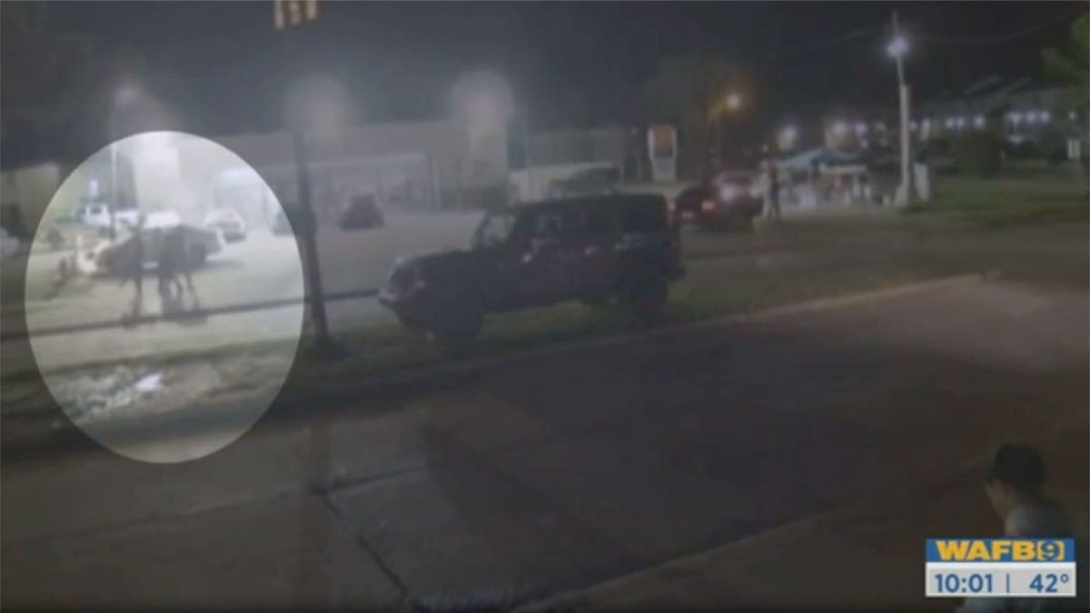 Security footage of a young woman walking behind four men in a busy parking lot.