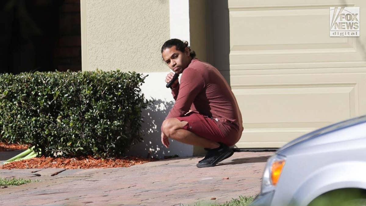 Man crouching, shaving in the driveway of his home