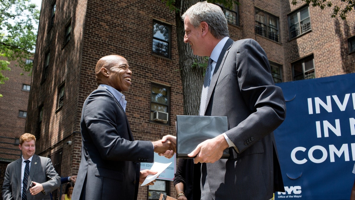 Mayor Eric Adams shakes hands with former Mayor Bill de Blasio