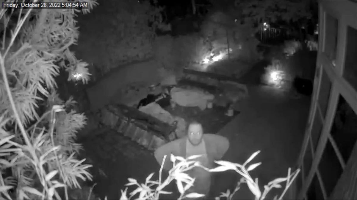 Black and white security footage of a man in a backyard.