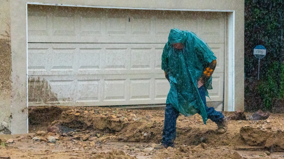 A man in heavy rain jumps over mudslide and rushing water in Studio City, Calif.