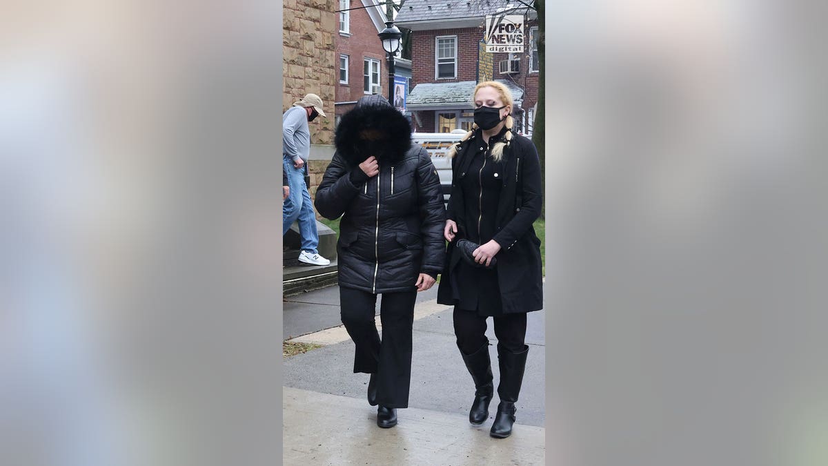 A woman with a black coat on with fur-lined hood pulled over her face walks alongside a younger woman