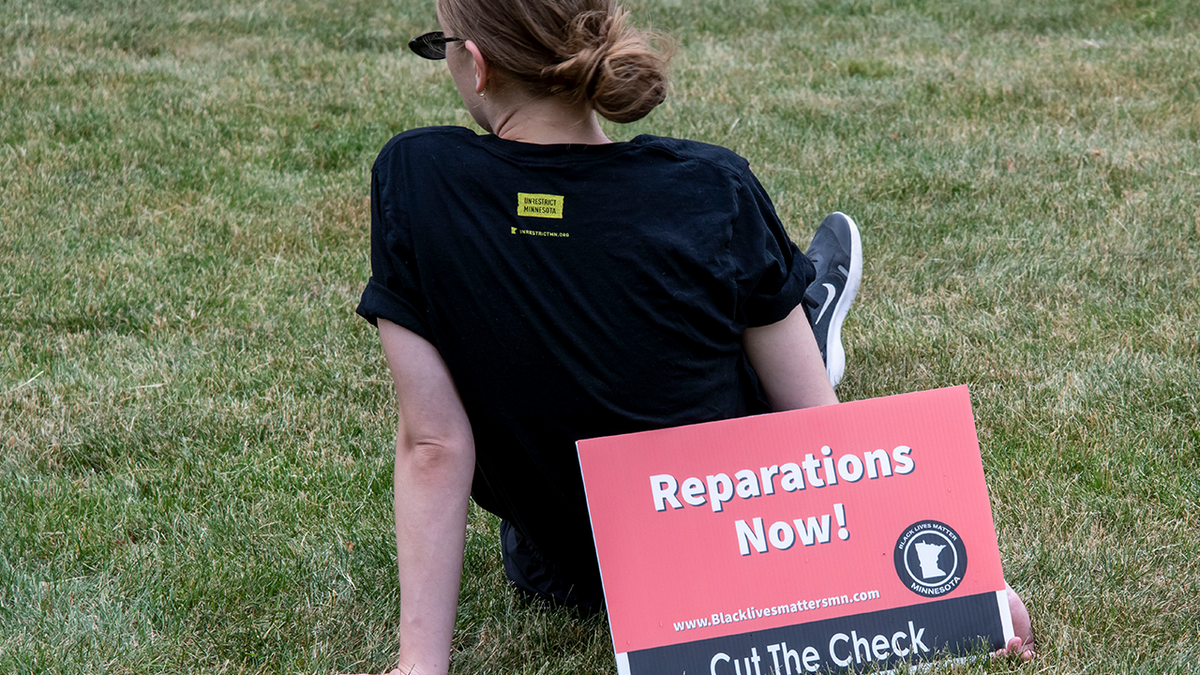 Woman holds a Reparations Sign