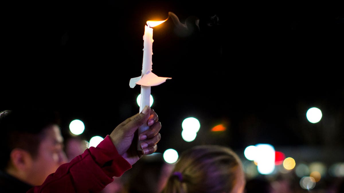A hand holds up a candle at a vigil in honor of Abigail Zwerner, the Virginia teacher shot by her student