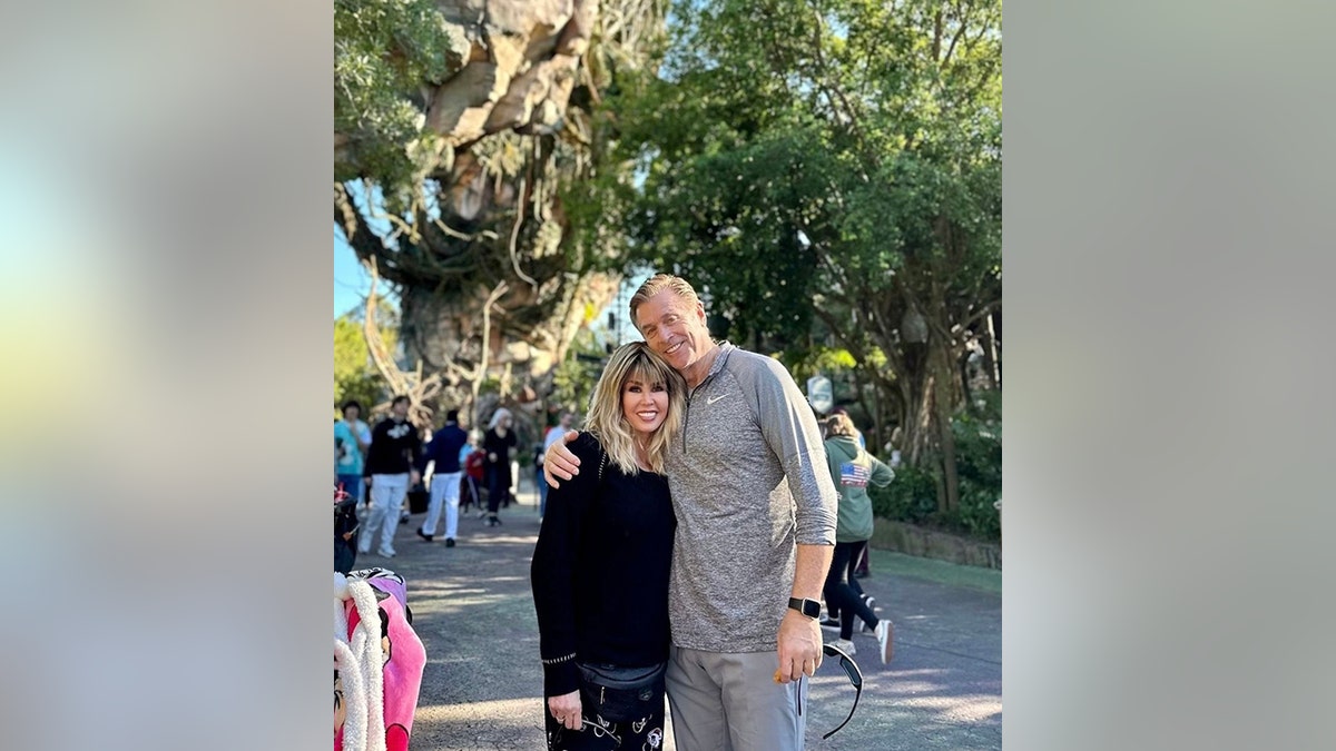 Marie Osmond in black smiles next to her husband Steve Craig in a grey Nike zip-up with a blonde wig on at Disney World