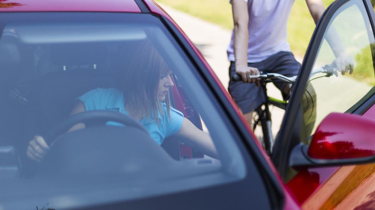 Woman opens car door while biker approaches