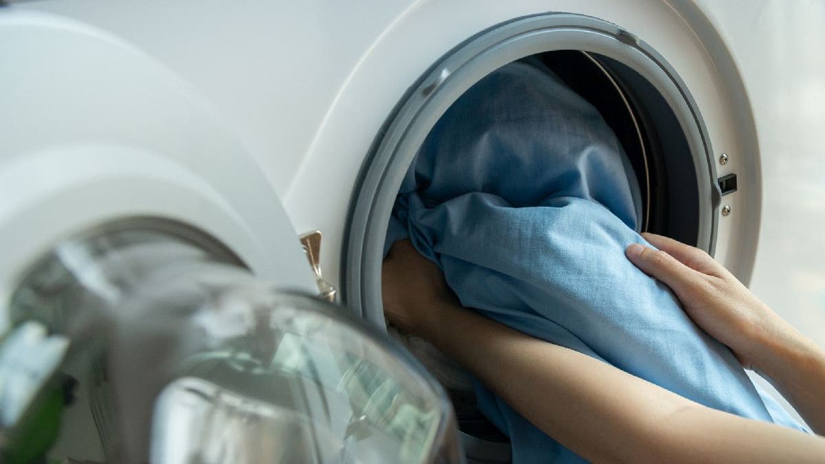 Mulher coloca lençóis na máquina de lavar