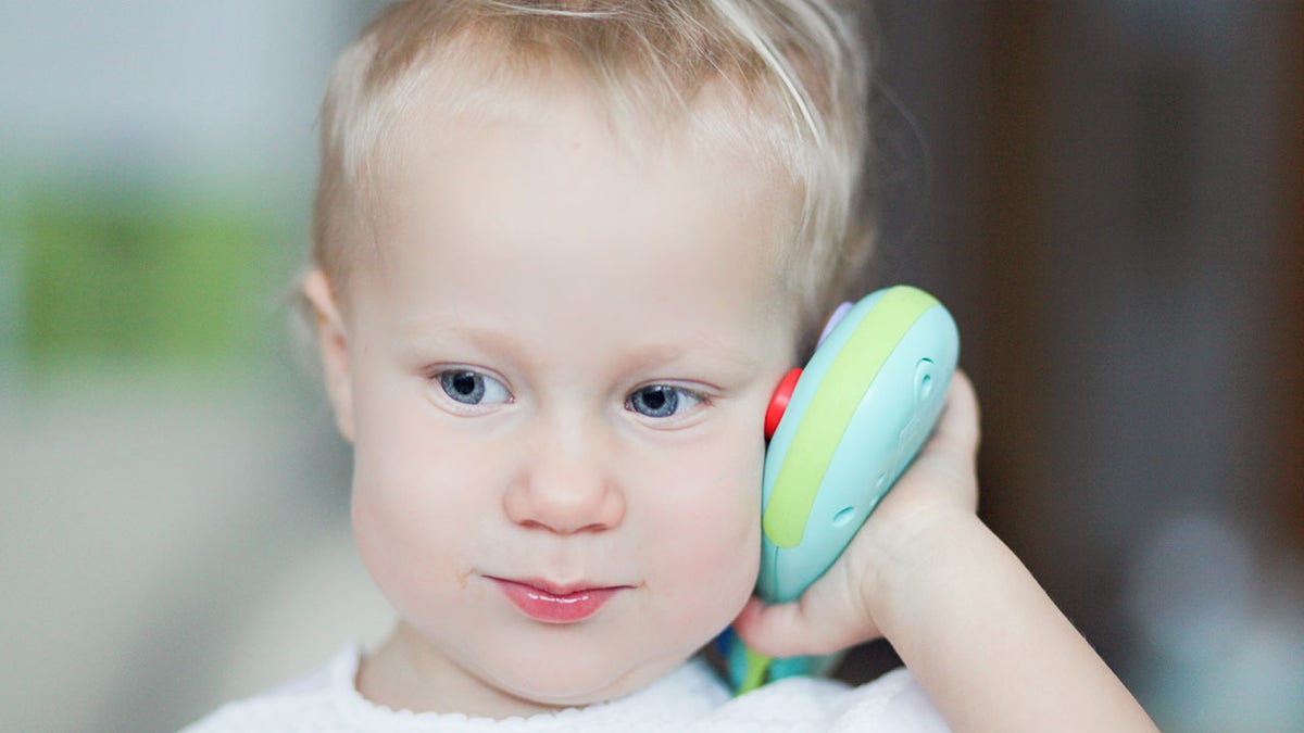 baby holds toy phone to ear