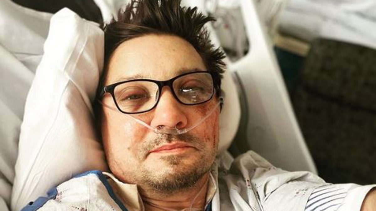 Jeremy Renner sent from the hospital after the accident wearing dark rimmed glasses, a breathing tube in the nose and a hospital gown with bruises on the face.