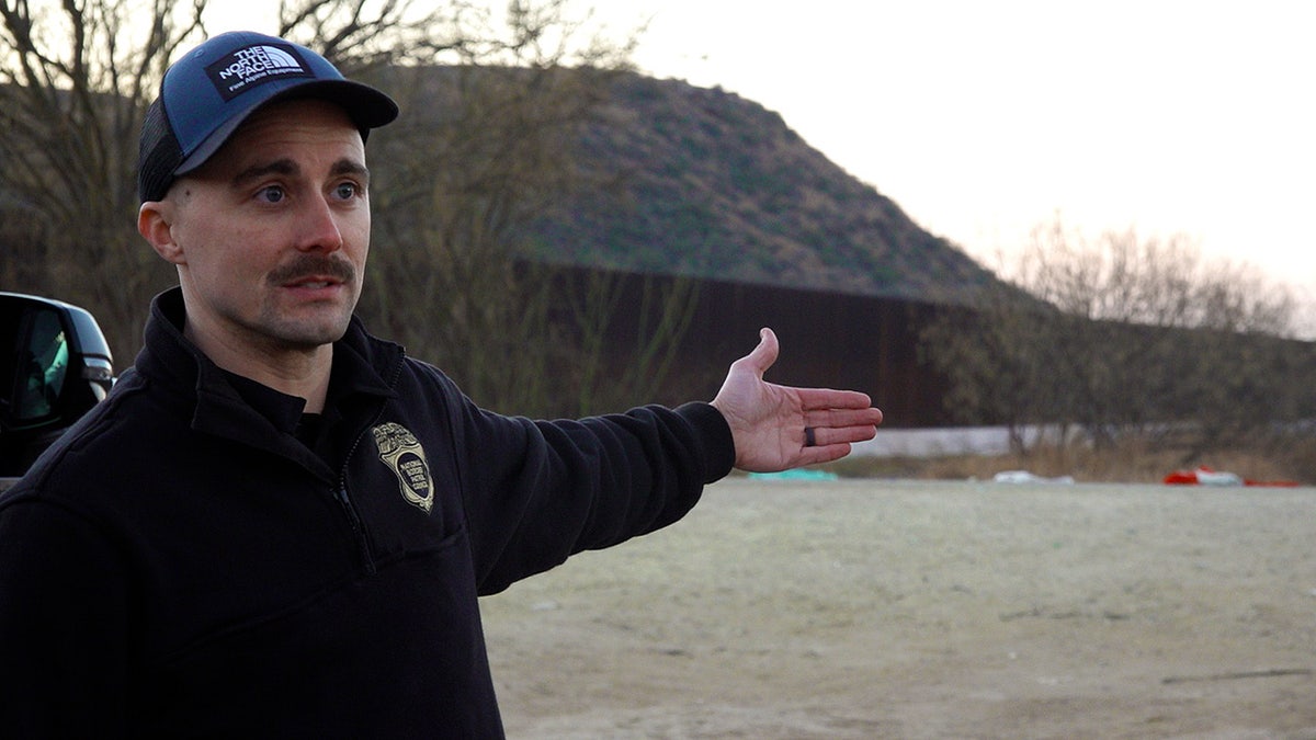 border patrol agent stands in front of fence