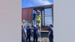 Firefighters pull migrants from a rail car carrying cases of Corona Extra beer