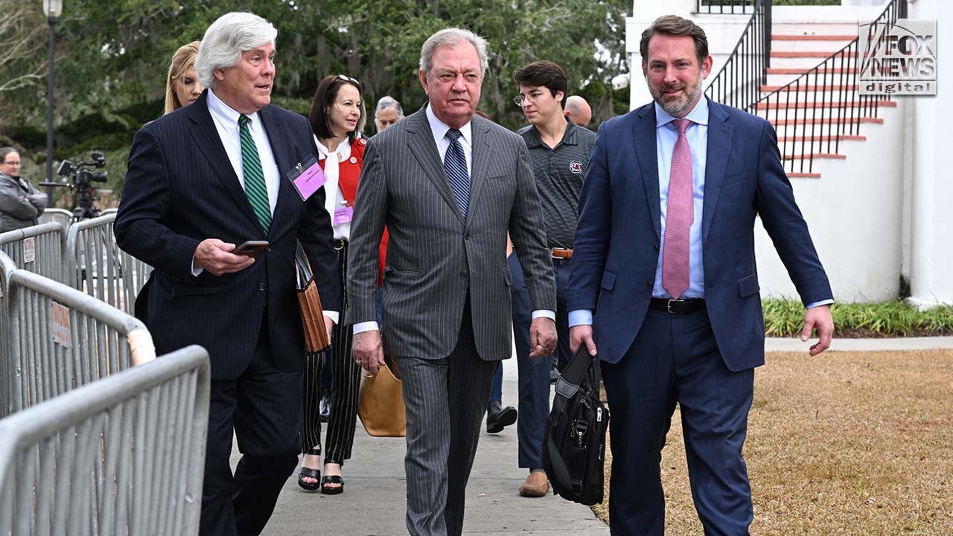 Three men wearing suits walk outside a courthouse.