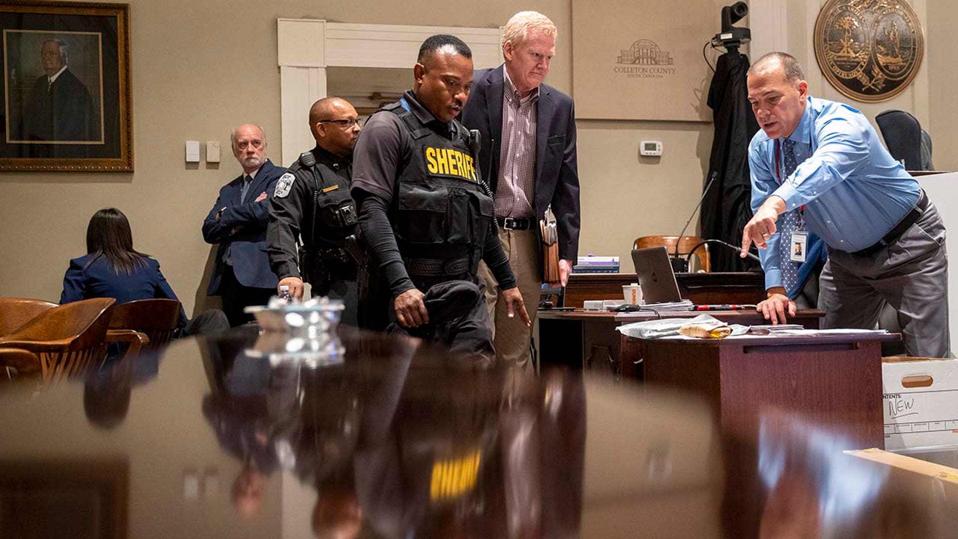 Police officers lead a man into a courtroom.