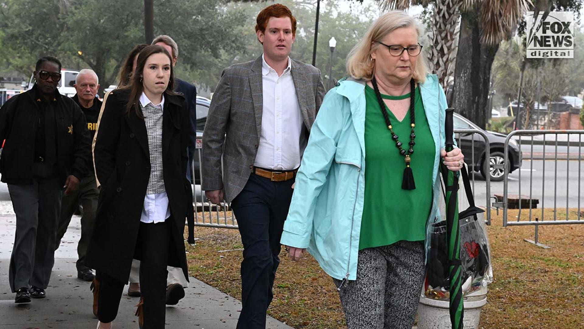 A group of people walk on a sidewalk, into a courthouse.