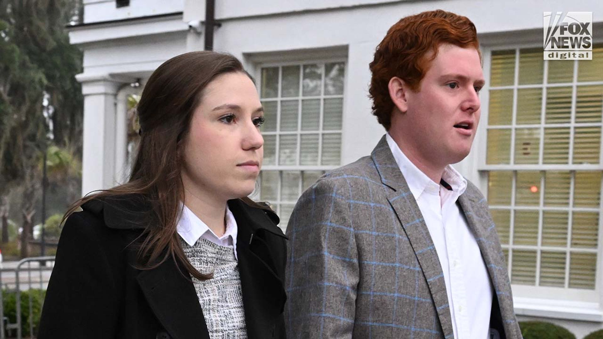 A man wearing a suit and a woman wearing a coat enter a courthouse.