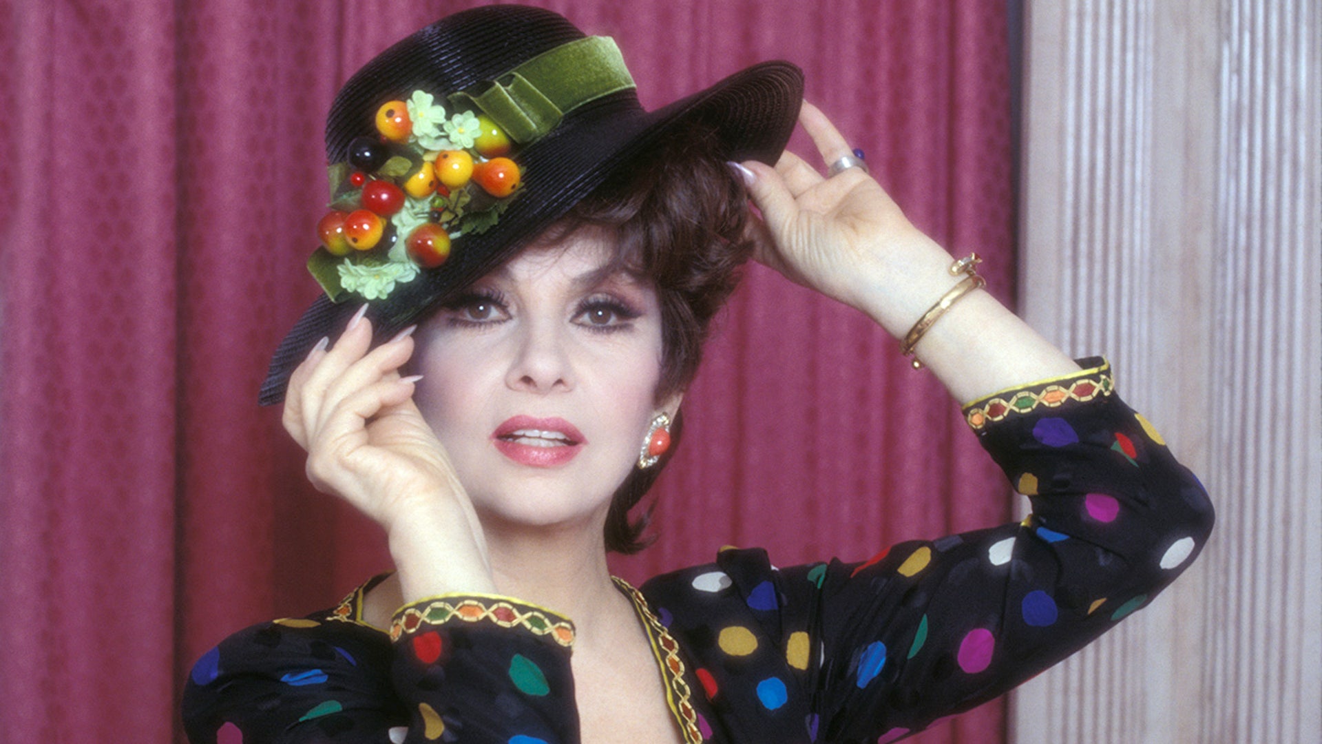 Gina Lollobrigida in a black hat with fruit on it and black shirt with colorful polka dots