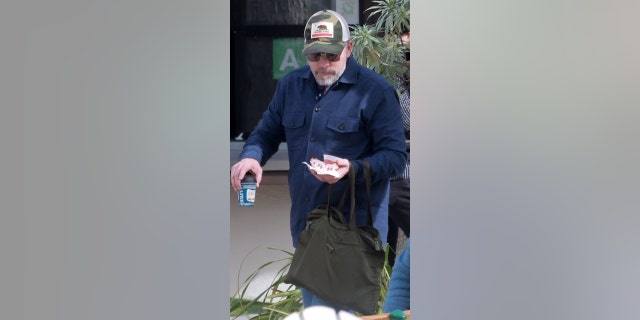 A man in a trucker hat and sunglasses carries food.