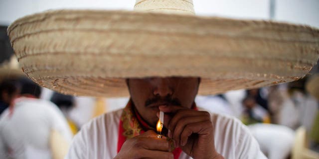 Ein Mann in traditioneller mexikanischer Kleidung zündet sich eine Zigarette an, während er sich auf eine Parade während der Gedenkfeier zum 112. Jahrestag der mexikanischen Revolution auf dem Zocalo-Platz in Mexiko-Stadt am 20. November 2022 vorbereitet.