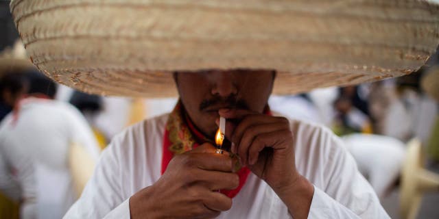 A man wearing a traditional Mexican lights a cigarrette as he prepares to parade during the commemoration the 112th anniversary of the Mexican Revolution at the Zocalo square in Mexico City, on Nov. 20, 2022.