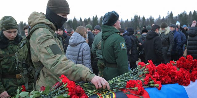 A man places flowers at the coffin during the funeral of Dmitry Menshikov, a mercenary for the private Russian military company Wagner Group killed during the military conflict in Ukraine, in the Alley of Heroes at a cemetery in Saint Petersburg, Russia, Dec. 24, 2022. 
