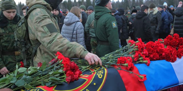 Wagner Group mercenary lays flowers on casket