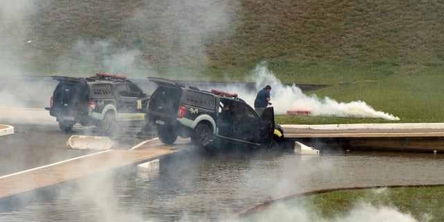 Police cars are pictured amidst tear gas after being pushed off the road by supporter of Brazil's far-right former President Jair Bolsonaro who dispute the election of leftist President Luiz Inacio Lula da Silva, during protests, in Brasilia, Brazil Jan. 8, 2023.