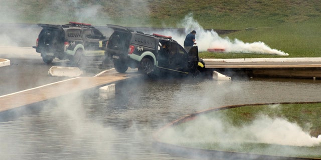 Police cars are pictured amidst tear gas after being pushed off the road by supporter of Brazil's far-right former President Jair Bolsonaro who disputes the election of leftist President Luiz Inacio Lula da Silva, during protests, in Brasilia, Brazil Jan. 8, 2023.