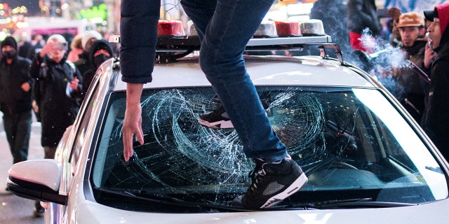 A protestor steps on the windshield of a police vehicle, on the day of the release of a video showing police officers beating Tyre Nichols, the young Black man who died three days after he was pulled over while driving during a traffic stop by Memphis police officers, in New York, U.S., January 27, 2023.