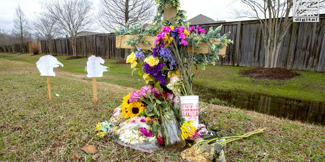 A small wooden cross covered with flowers by the side of a highway