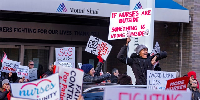 A supporter stands through the sunroof of a passing vehicle in front of Mt. Sinai Hospital in the Manhattan borough of New York Monday, Jan. 9, 2023, as nurses stage a strike following the breakdown of negotiations with the hospital hours earlier. 