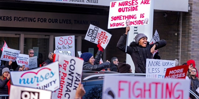 A supporter stands through the sunroof of a passing vehicle in front of Mt. Sinai Hospital in the Manhattan borough of New York Monday, Jan. 9, 2023, as nurses stage a strike following the breakdown of negotiations with the hospital hours earlier. 