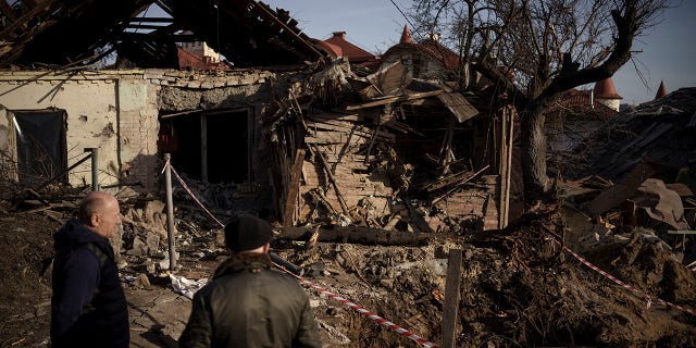 People stand next to the site of a Russian attack in Kyiv, Ukraine, Monday, Jan. 2, 2023.