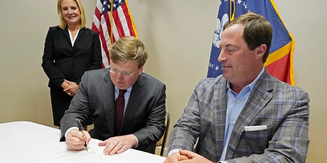 With wife Elee Reeves, left, and party Chairman Frank Bordeaux witnessing, Mississippi Gov.  Tate Reeves, center, signs his qualifying papers to run for re-election at the party headquarters in Jackson Jan. 3, 2023.