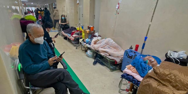 People wearing face masks scroll through their phones and look at their elderly relatives receiving intravenous drips in the corridor of a Beijing hospital on January 5, 2023.