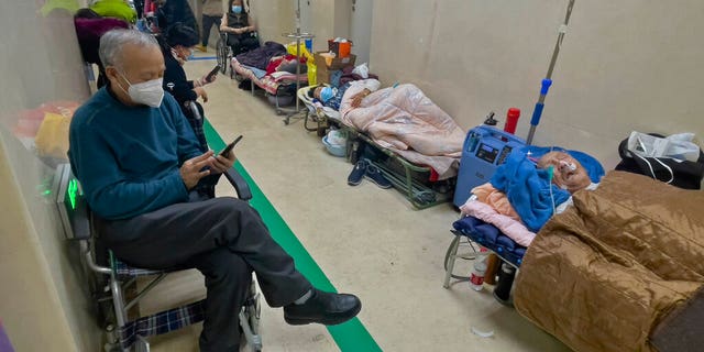 People wearing face masks browse their phones and look on as their elderly relatives receive intravenous drips in a Beijing hospital corridor on Jan. 5, 2023.