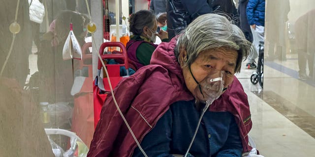 An elderly patient receives an intravenous drip while using a ventilator in the corridor of a Beijing hospital on January 5, 2023.