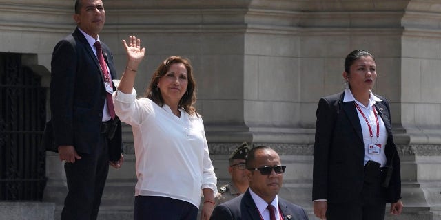 Surrounded by security, Peruvian President Dina Boluarte waves to the press outside the government palace as Prime Minister Alberto Otarola departs in Lima, Peru, Tuesday, Jan. 10, 2023.