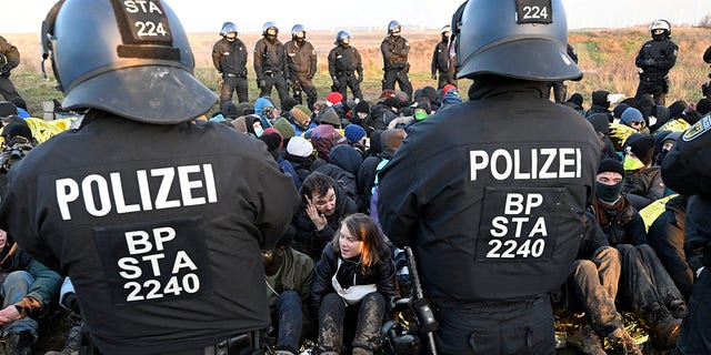 Police officers stand in front of a group of protesters, including Swedish climate activist Greta Thunberg, center bottom, on the edge of the Garzweiler II opencast lignite mine during a protest action by climate activists after the clearance of Luetzerath, Germany, Tuesday, Jan. 17, 2023. 