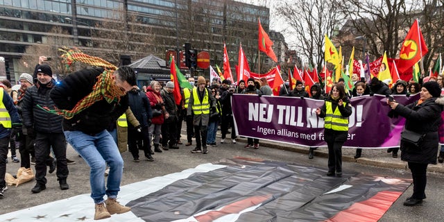 A protester prepares to jump on a banner with the image of Turkish President Recep Tayyip Erdogan during a demonstration organized by The Kurdish Democratic Society Center in Sweden, as Sweden seeks Turkey's approval to join NATO, in Stockholm, Saturday, January 21 2023. (Christine Olsson/TT Nyhetsbyrå via AP)